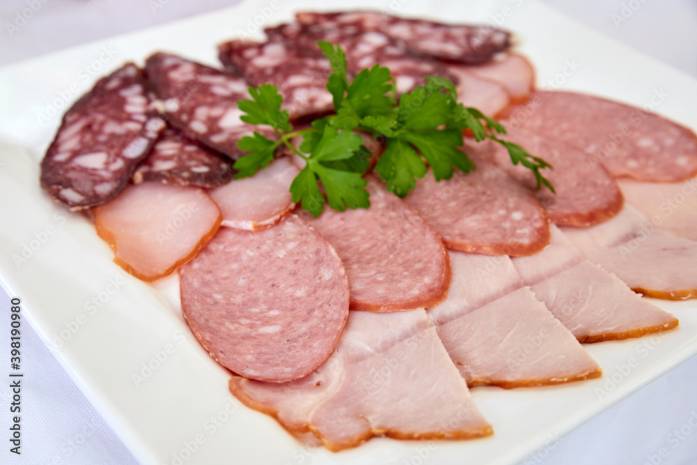 Cold cuts with parsley on a white plate. Close-up, selective focus