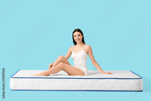 Young woman sitting on mattress against color background