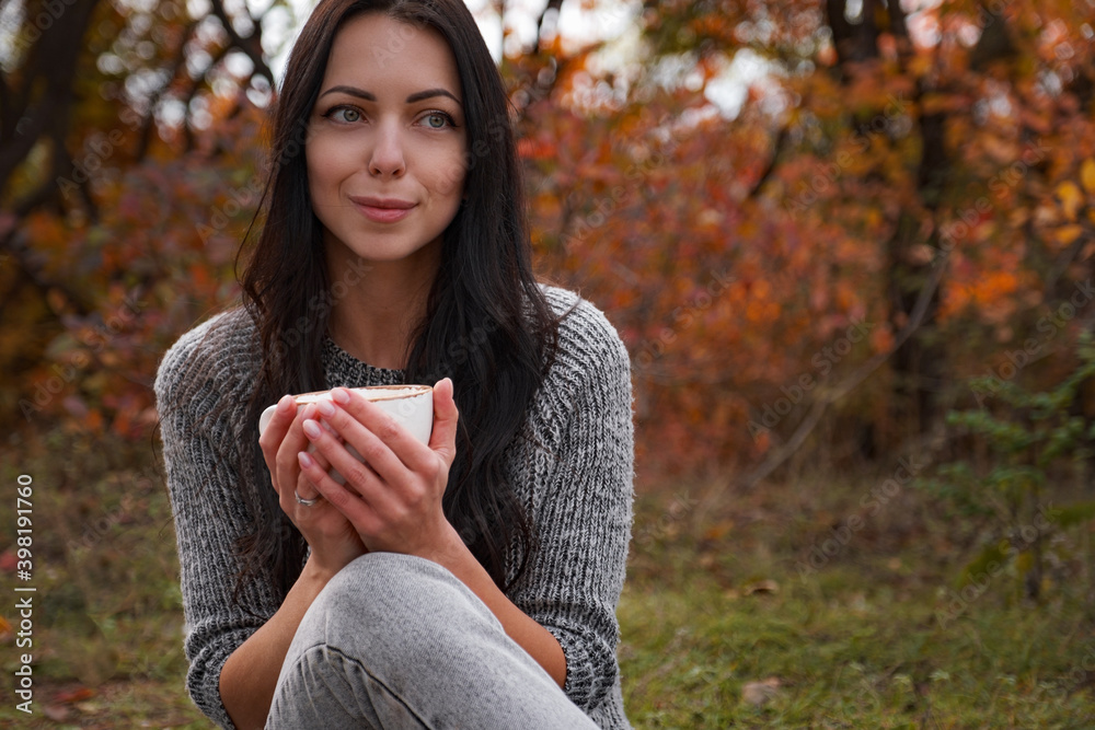 Woman in cozy sweater holding a cup with hot drink . Tea time outdoors.