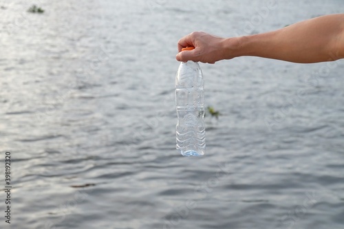 A man hand holding a plastic bottle of drinking water into a river with water background for an environmental cleaning concept  photo