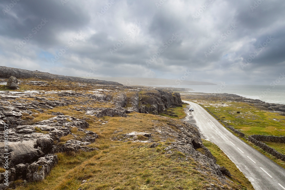 Landscape in Burren area by Atlantic ocean, West of Ireland. Small narrow asphalt road by the ocean, part of Wild Atlantic Way route. Beautiful cloudy sky. Travel and nature concept. Landscape in Burren area by Atlantic ocean, West of Ireland. Small narrow asphalt road by the ocean, part of Wild Atlantic Way route. Beautiful cloudy sky. Travel and nature concept.