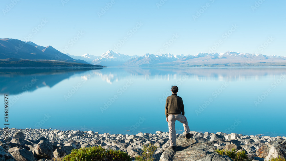 Tourist standing on the shore of Lake Pukaki, watching Mt Cook reflected in the clear waters Tourist standing on the shore of Lake Pukaki, watching Mt Cook reflected in the clear waters
