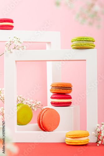 Colorful french macaron dessert. Set of various different tastes and color macaroon cookies with square shapes and flowers on pink background. Festive greeting card concept with copy space