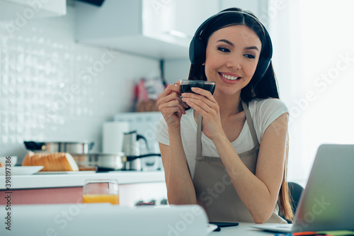 Mirthful lady wearing an apron relaxing in the kitchen with coffee