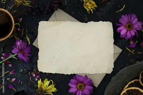 Mockup of letter on an envelope among wilted flowers, a cup of coffee and a vintage plate. Top view. Melancholic mood