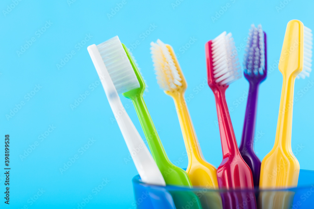 A group of colorful toothbrushes in a blue glass. Studio photo isolated on blue background. Selective focus on object. A group of colorful toothbrushes in a blue glass. Studio photo isolated on blue background. Selective focus on object.