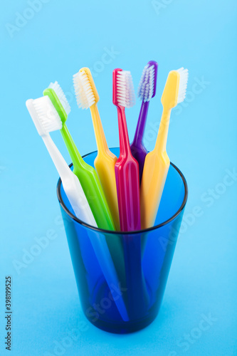 A group of colorful toothbrushes in a blue glass. Studio photo isolated on blue background. Selective focus on object. 