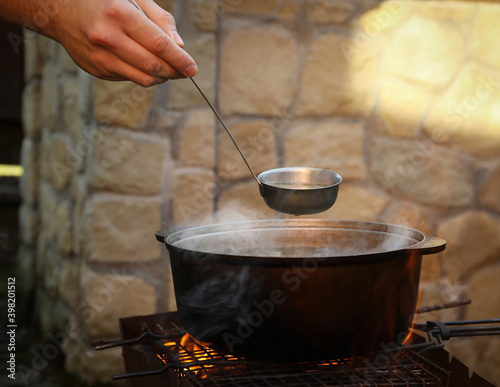 Man holding ladle over metal cauldron with soup on fire photo