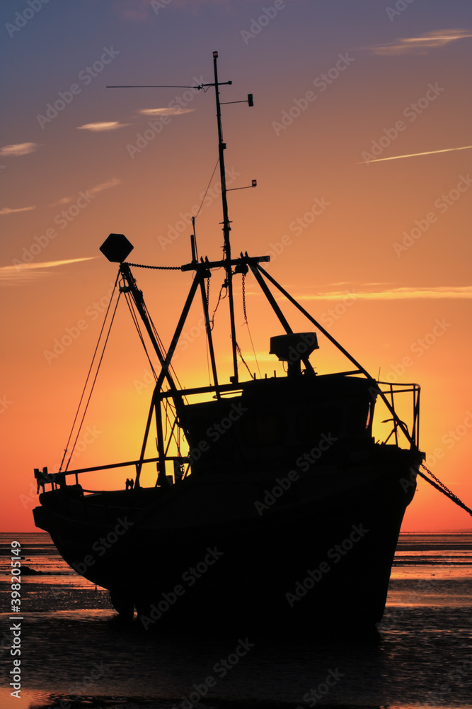 Beached boat in silhouette against sun at dawn or sunset