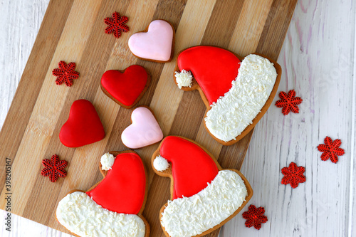 Christmas sweet cookies, gingerbread cookies in the form of red Santa Claus cap and heart with icing lie, New Year decorations on wooden background. Festive homemade food