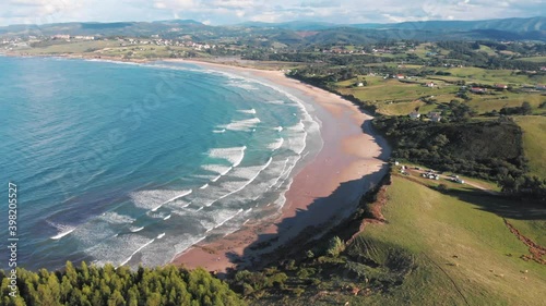 Aerial drone shot of the Cantabrian coast through San Vicente de la Barquera and the Oyambre Natural Park. Mountains and green cliffs by the sea, where you will find famous beaches for surfing. Waves