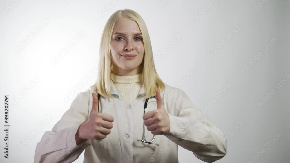 Doctor thumb up. Friendly woman doctor in white coat and stethoscope on white backgrounds looks at camera
