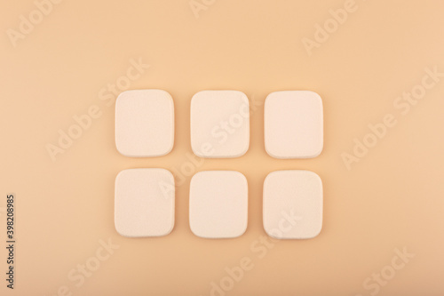 Two rows of square beige make up sponges on beige background