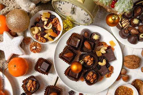 Fototapeta Naklejka Na Ścianę i Meble -  sweet food background for christmas or holiday decoration - chocolate candies, tangerines, nuts and dried fruits on white wood