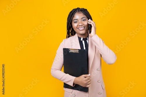 beautiful young female in a jacket with a folder on a yellow background with a mobile phone photo