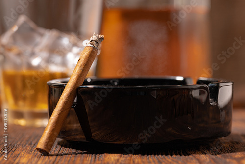 Glass of whisky and lighted cigar in an ash tray