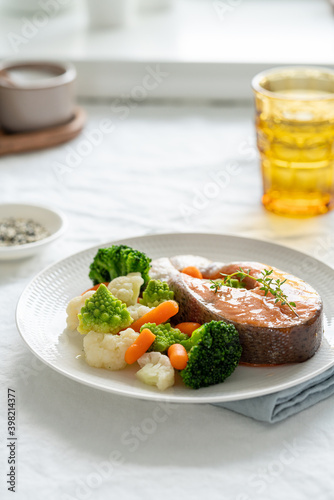 Steam salmon and vegetables, Paleo, keto, fodmap, dash diet. Side view, vertical. Mediterranean diet with steamed fish. Healthy concept, white plate on gray table, gluten free, lectine free