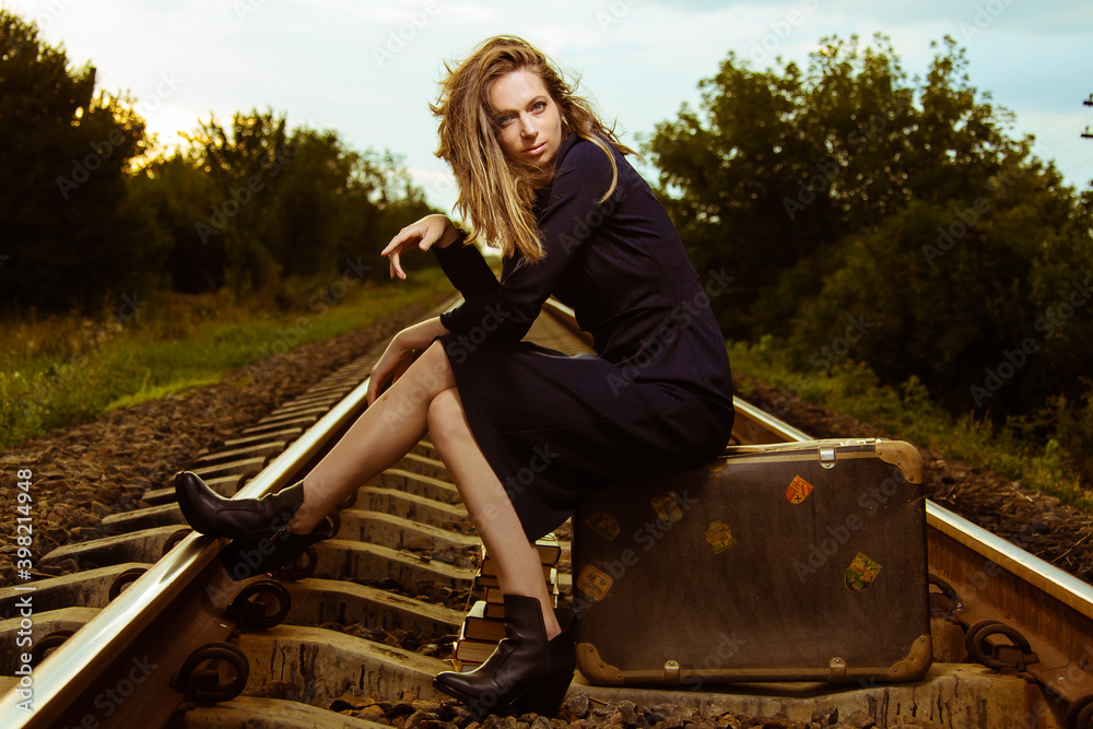 A girl sitting on a suitcase on the railroad