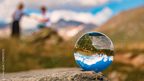 Crystal ball alpine summer landscape shot with a flirting couple at the famous Timmelsjoch high alpine road, Dolomites, South Tyrol, Italy