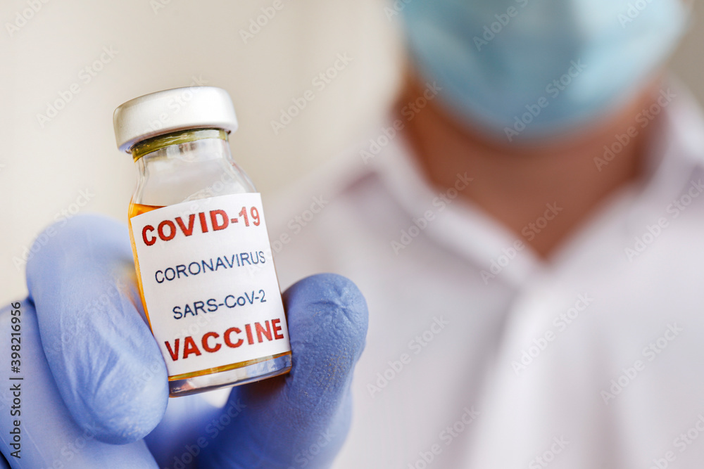 Macro shot of a doctor wearing face mask and latex gloves demonstrating the new covid-19 vaccine in vial. Close up portrait, copy space, background.