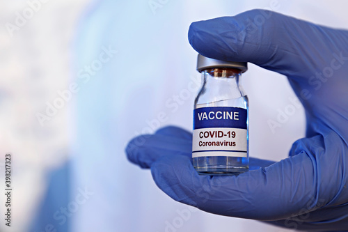 Macro shot of doctor's hands in blue latex gloves showing the new covid-19 vaccine vial. Close up, copy space, background.