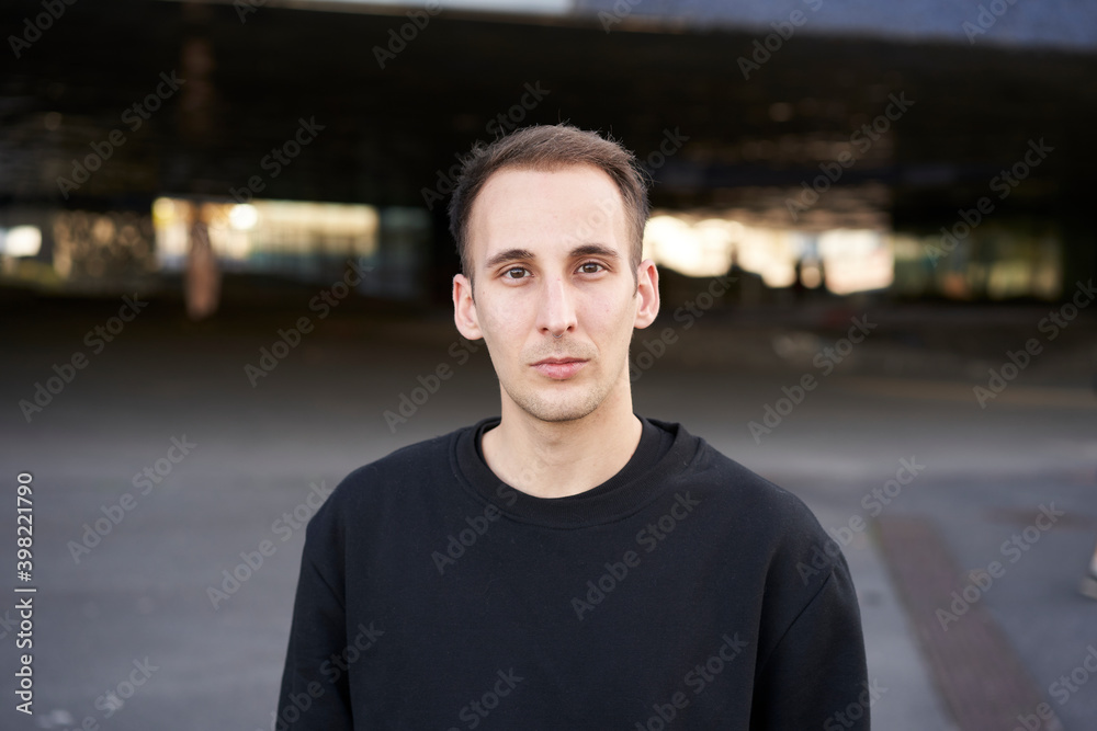 Looking to the camera. Portrait of a serious Hispanic young man while standing in a city. Looking to the camera. Portrait of a serious Hispanic young man while standing in a city.