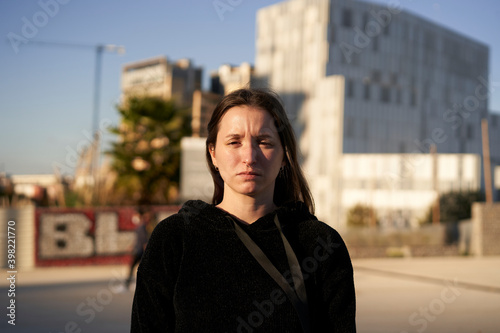 Looking to the camera. Portrait of a serious Hispanic young woman while standing in a city. © CarlosBarquero