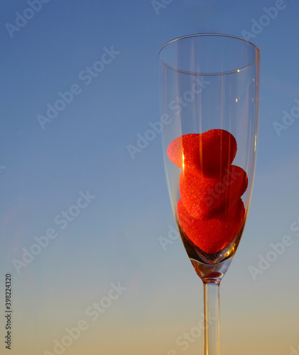 Red jelly hearts in glass of champagne on blue sky background with copy space, vertical image, selective focus photo