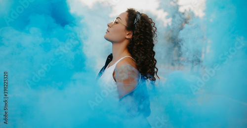 Portrait of young woman against background of blue smoke. photo