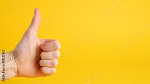 Hand thumbs up sign on yellow background. Confirm gesture. Left side. Accept gesture and approve sign
