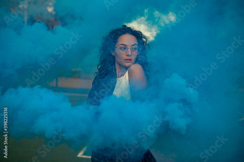 Young woman stands against background of blue smoke.