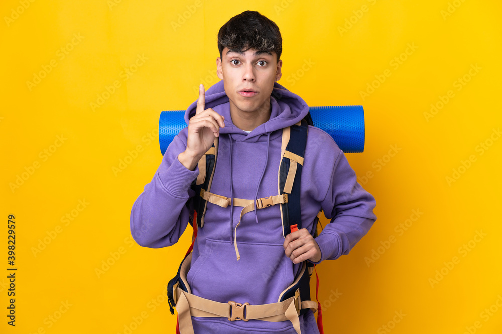 Young mountaineer man with a big backpack over isolated yellow background intending to realizes the solution while lifting a finger up Young mountaineer man with a big backpack over isolated yellow background intending to realizes the solution while lifting a finger up