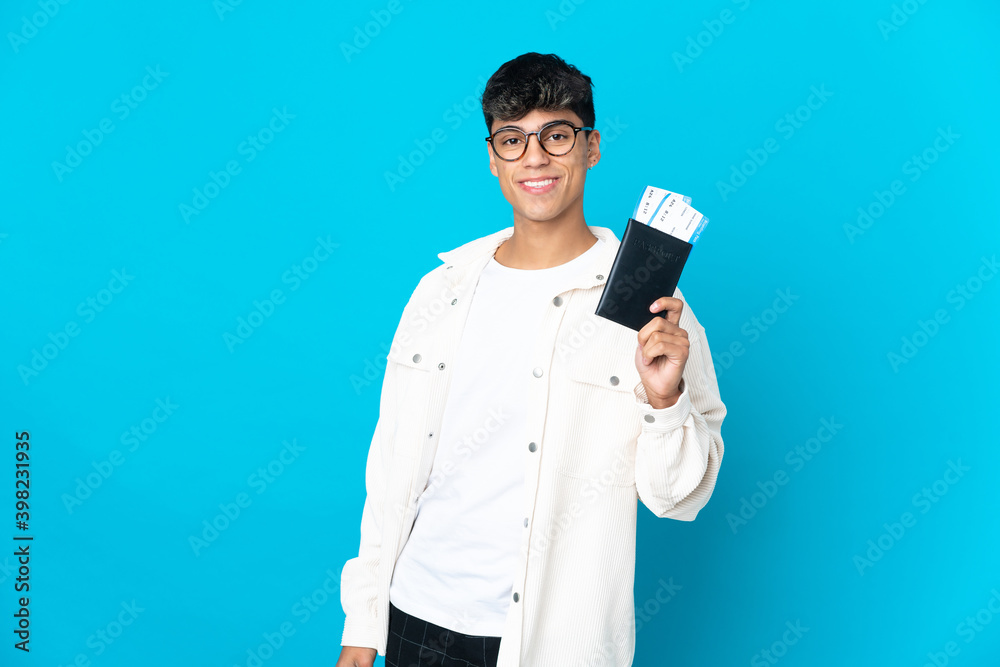 Young man over isolated blue background happy in vacation with passport and plane tickets