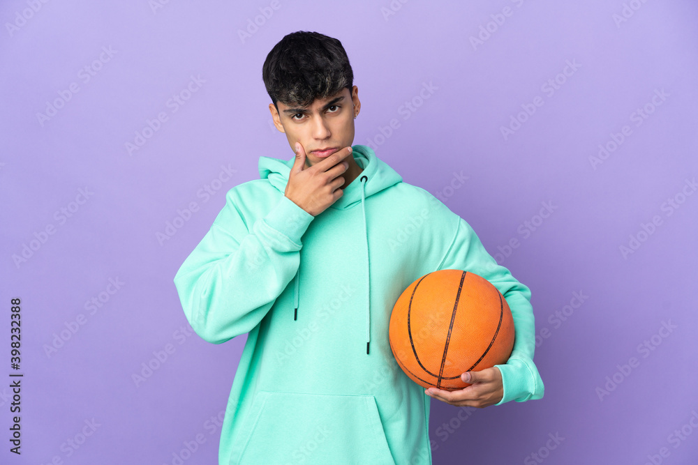 Young man playing basketball over isolated purple background thinking