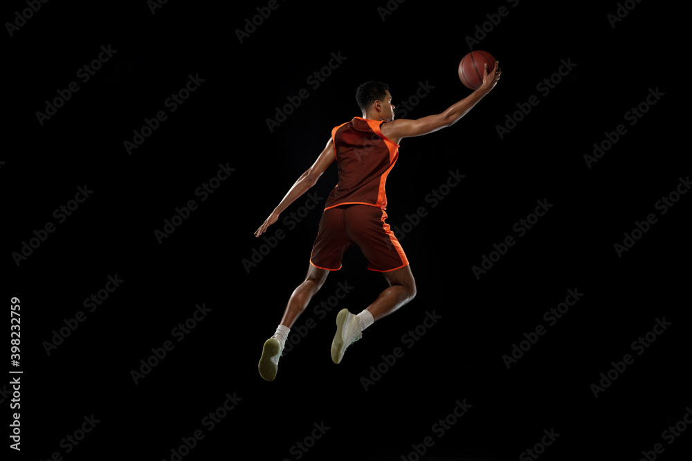 Flying. Young purposeful african-amrican basketball player training, practicing in action, motion isolated on black background. Concept of sport, movement, energy and dynamic, healthy lifestyle.