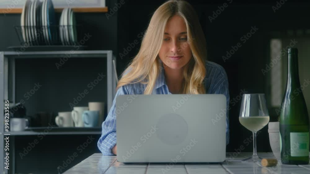 Beautiful young woman browse internet and social media on laptop in kitchen. Freelancer or writer blogger work on new project or article, sip wine. Copy space and clean shot of work from home office Beautiful young woman browse internet and social media on laptop in kitchen. Freelancer or writer blogger work on new project or article, sip wine. Copy space and clean shot of work from home office