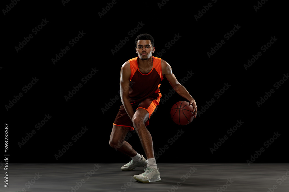 Leading. Young purposeful african-amrican basketball player training, practicing in action, motion isolated on black background. Concept of sport, movement, energy and dynamic, healthy lifestyle.