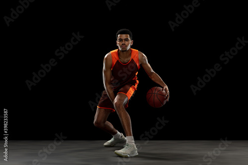 Leading. Young purposeful african-amrican basketball player training, practicing in action, motion isolated on black background. Concept of sport, movement, energy and dynamic, healthy lifestyle.