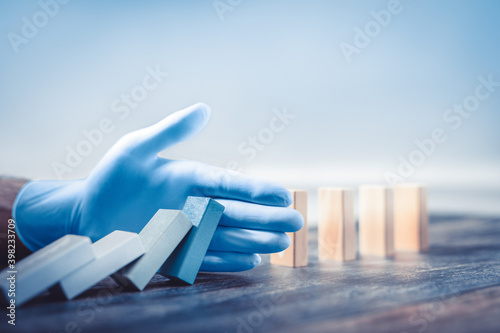 Hand with protective glove stopping domino effect.