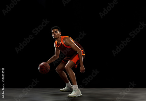 Winner. Young purposeful african-amrican basketball player training, practicing in action, motion isolated on black background. Concept of sport, movement, energy and dynamic, healthy lifestyle.