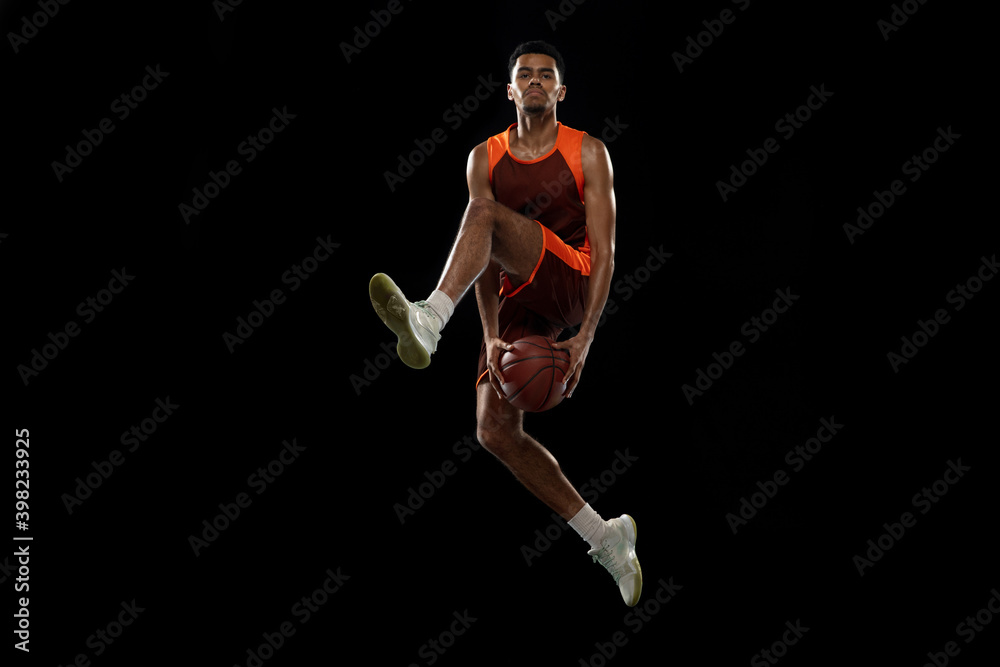 Flying. Young purposeful african-amrican basketball player training, practicing in action, motion isolated on black background. Concept of sport, movement, energy and dynamic, healthy lifestyle.