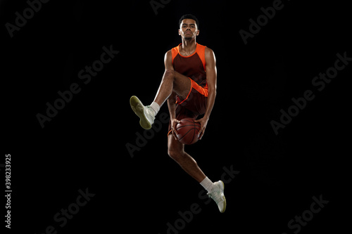 Flying. Young purposeful african-amrican basketball player training, practicing in action, motion isolated on black background. Concept of sport, movement, energy and dynamic, healthy lifestyle. © master1305