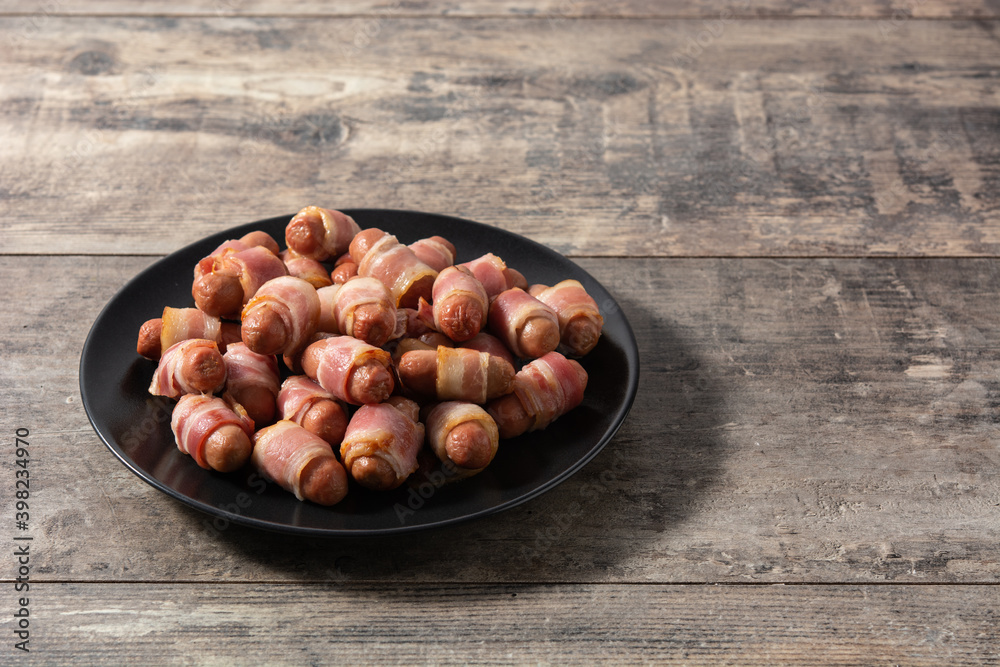Obraz premium Pig in blankets. Sausages wrapped in smoked bacon on wooden table 