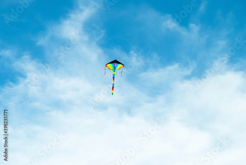 Rainbow color bright kite toy flying high up in blue sky background