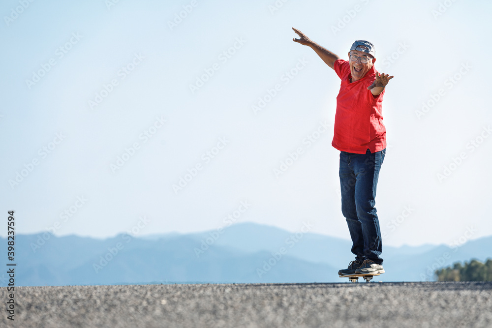 Uomo settantenne con polo rossa, va nel suo skateboard stando in equilibrio in una strada di campagna Uomo settantenne con polo rossa, va nel suo skateboard stando in equilibrio in una strada di campagna