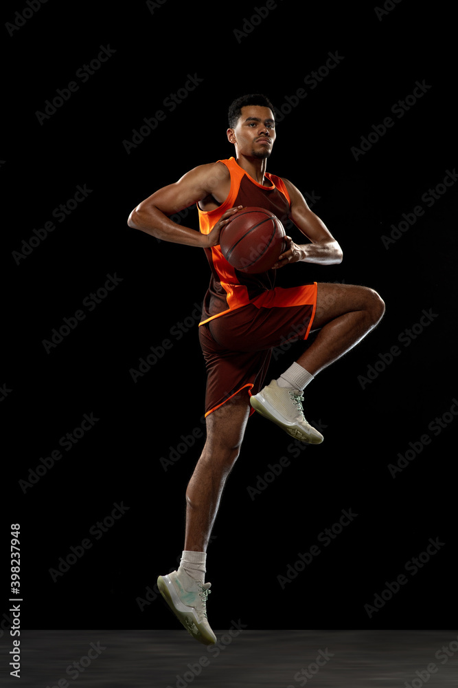 Jumping high. Young purposeful african-amrican basketball player training, practicing in action, motion isolated on black background. Concept of sport, movement, energy and dynamic, healthy lifestyle.