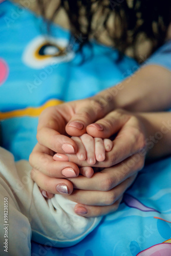 baby's hand in the hands of parents on the background of a garland and a Christmas tree