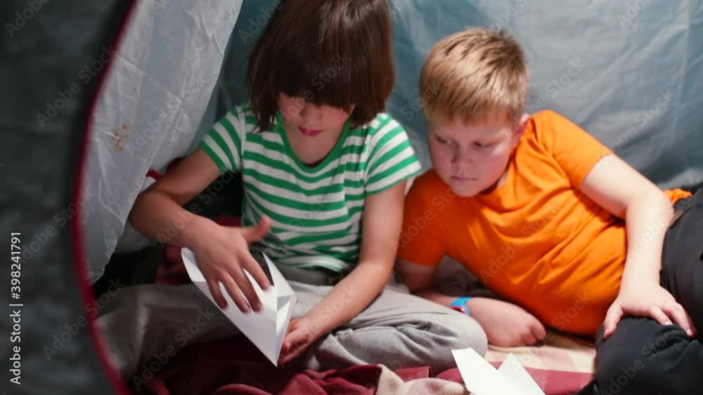 Two children in a tent are making origami paper. Fold the paper into a shape. Useful self-isolation entertainment. Two children in a tent are making origami paper. Fold the paper into a shape. Useful self-isolation entertainment.