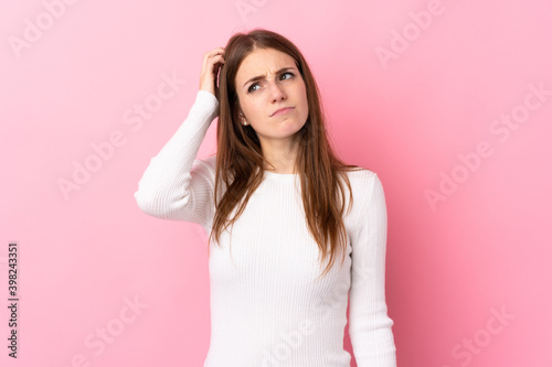 Young woman over isolated pink background having doubts while scratching head