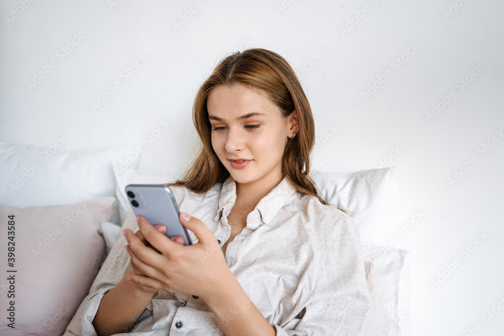 Beautiful pleased nice girl using cellphone while resting in bed Beautiful pleased nice girl using cellphone while resting in bed